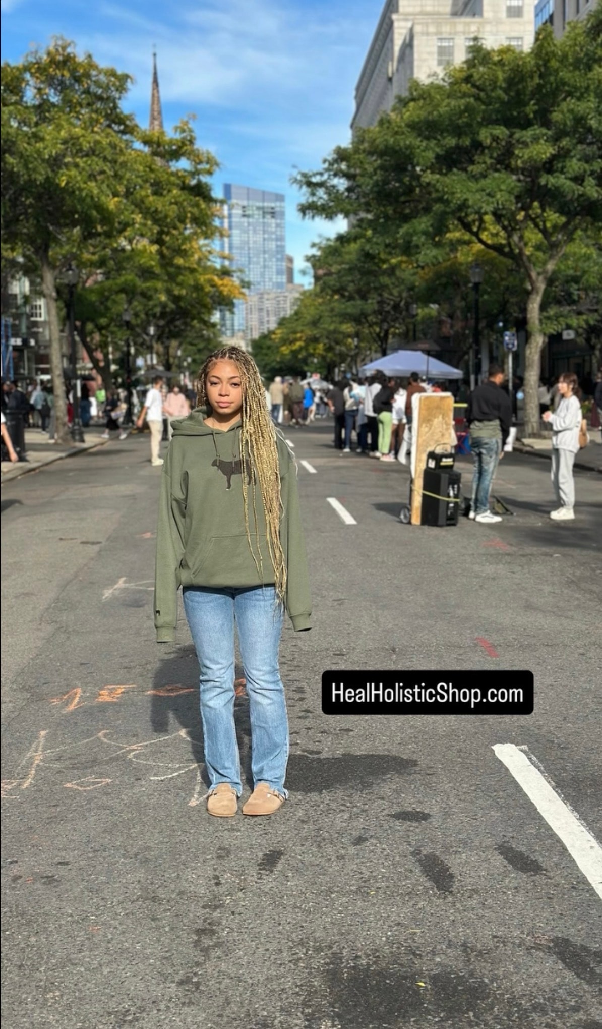 Person wearing Heal Holistic Shop army green hoodie on an urban street
